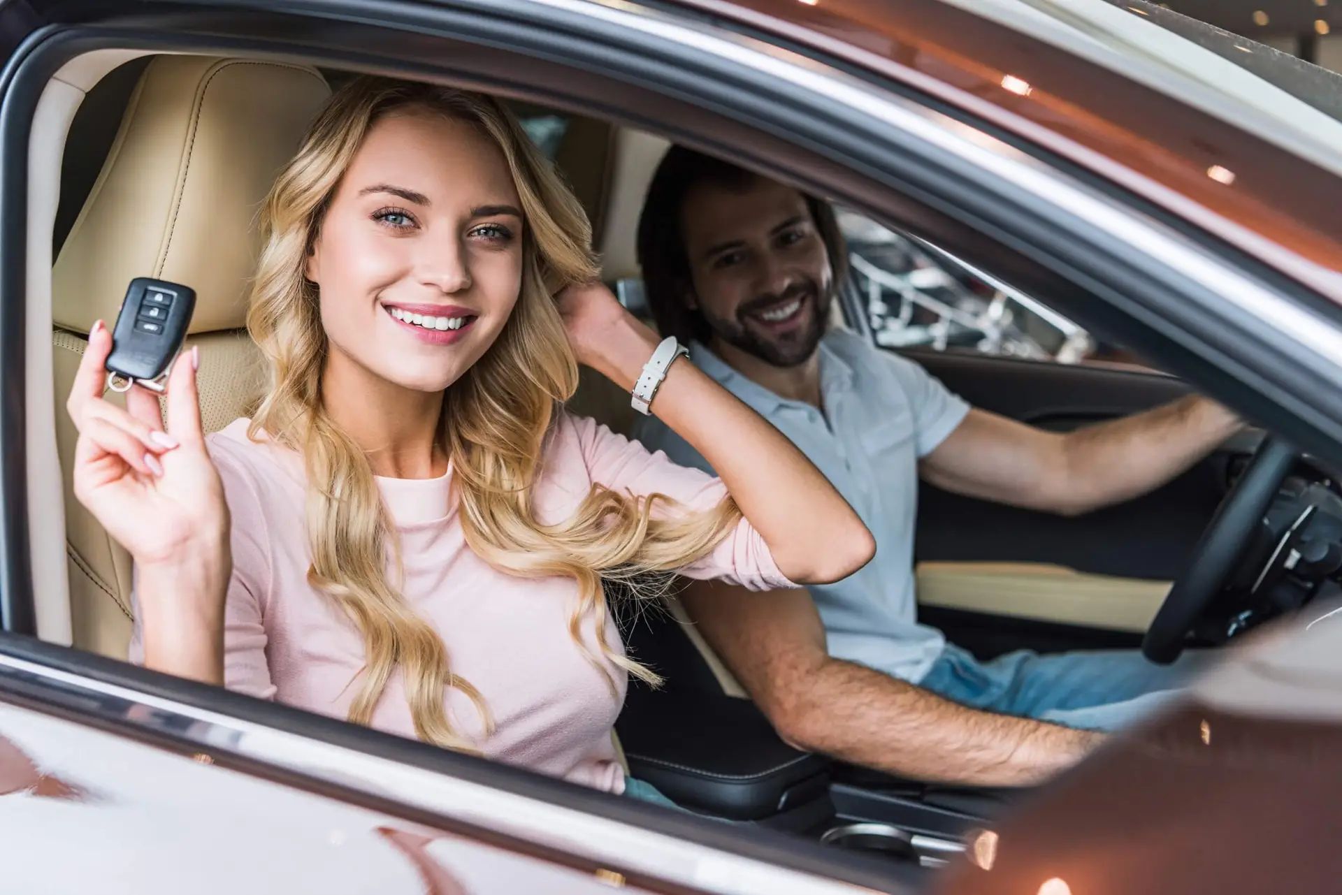 happy couple with car key in new automobile at dealership