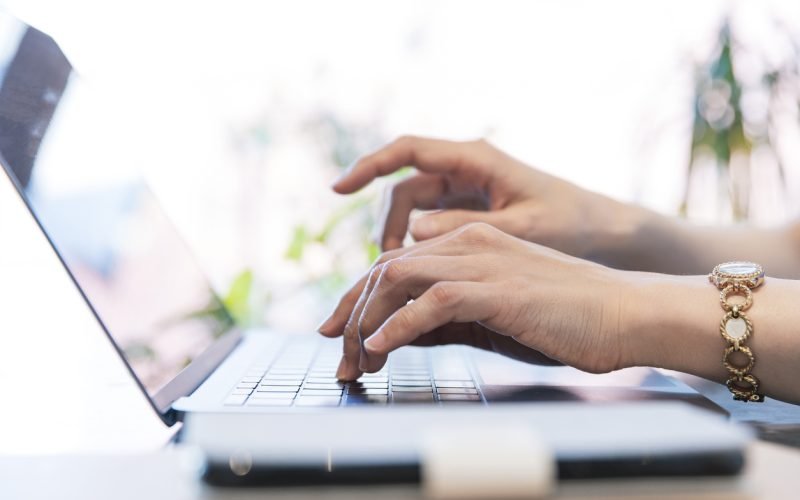 Close-up photo of female hands typing on keyboard at indoor workplace